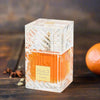 A square glass perfume bottle filled with amber-orange liquid, featuring a textured clear cap and a gold label reading 'Khamrah Lattafa'. It is set on a dark wooden surface with star anise and an orange in the background.