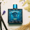 Blue Versace perfume bottle on a light background with flowers and vanilla beans.