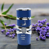 Blue perfume bottle with silver accents on a wooden surface with purple flowers and green leaves.