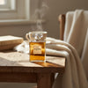 Chanel No. 5 perfume bottle on a wooden table with a cup and books in the background.