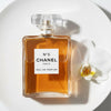 Chanel No. 5 perfume bottle with a white orchid on a white background