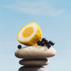 Half a lemon and blackberries on stacked stones with a clear blue sky background