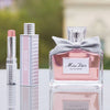 Miss Dior perfume bottle with a bow, lipstick, and other products on a reflective surface.