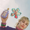 Person holding a floral perfume bottle with a close-up inset, wearing colorful jewelry.