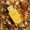 Shaghaf Vanilla Toffee perfume bottle surrounded by vanilla beans, nuts, and dates on a textured background.
